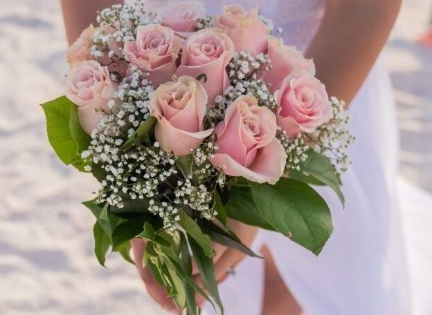 Bride holding pink rose bouquet on beach.