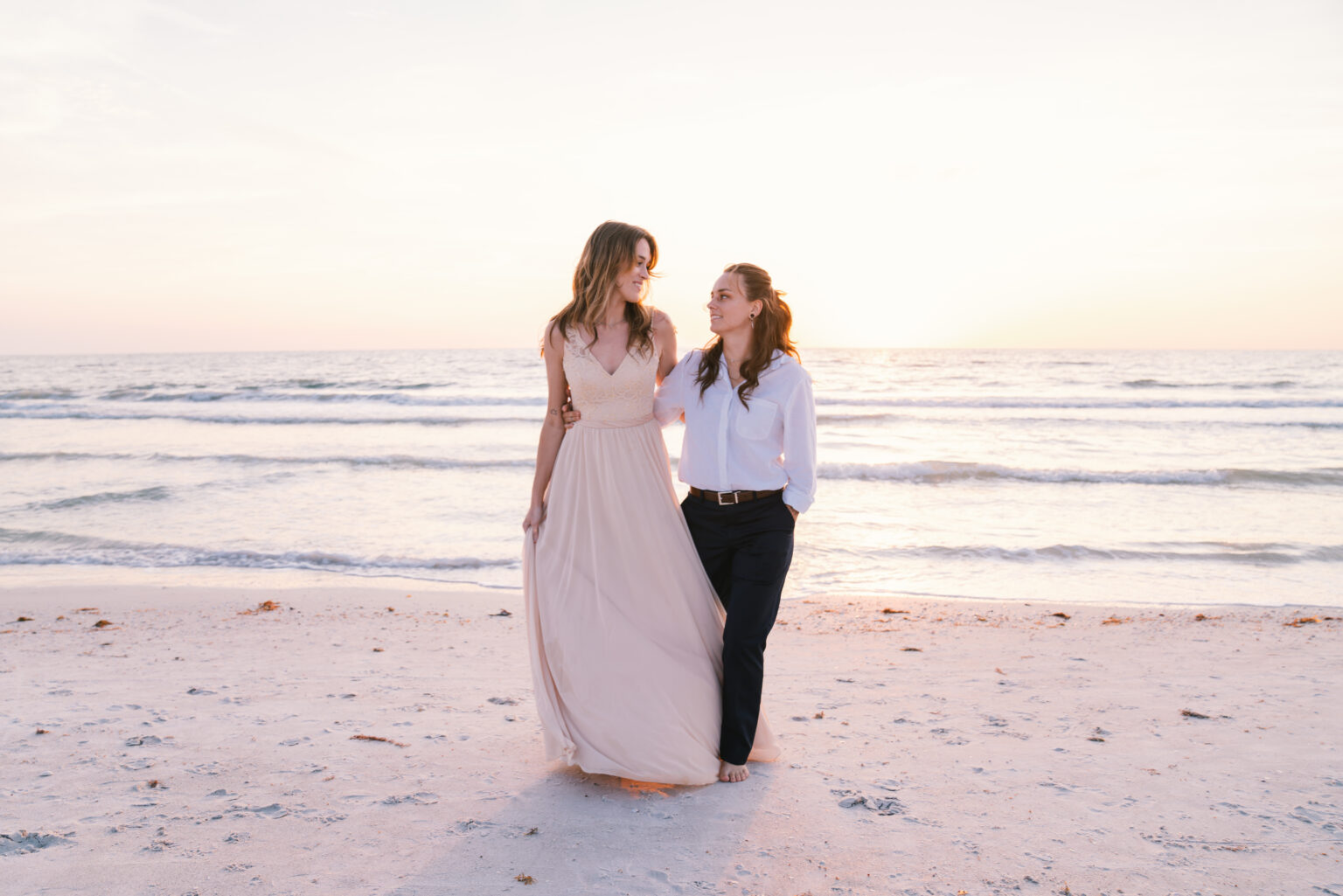 Two women smiling on a beach at sunset.